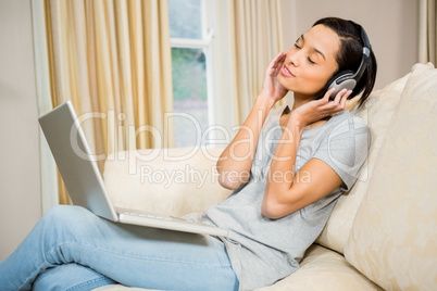 Smiling brunette using laptop and headphones