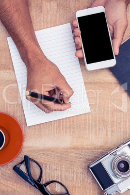 Businessman hand holding smart phone while writing on notepad