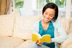 Smiling brunette reading book on the sofa