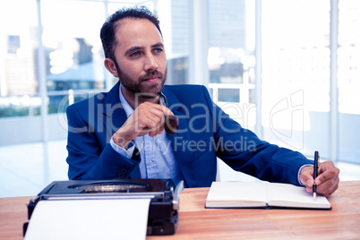 Thoughtful businessman holding pen while sitting at desk