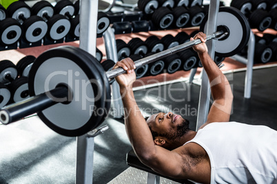 Muscular man lifting barebell while lying on bench