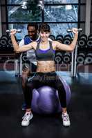 Male trainer helping woman during dumbbells exercise