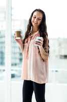 Smiling woman using smartphone holding disposable cup
