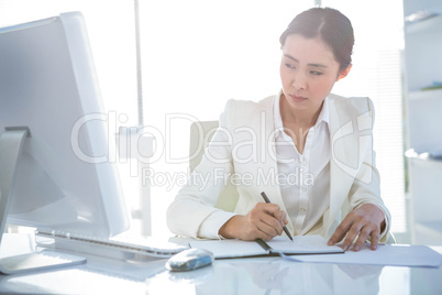 Businesswoman writing on diary on desk