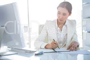 Businesswoman writing on diary on desk