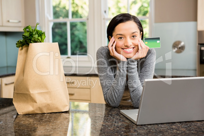 Smiling brunette in kitchen holding credit card