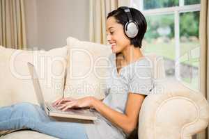 Smiling brunette using laptop and headphones