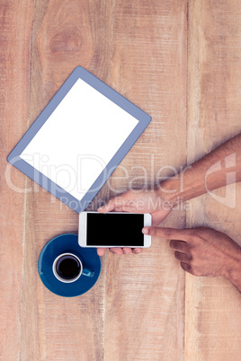 Man using smart phone by coffee and tablet on table