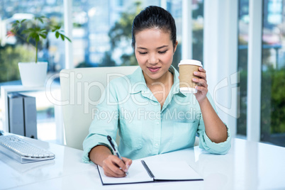 Smiling businesswoman writing notes with a coffee