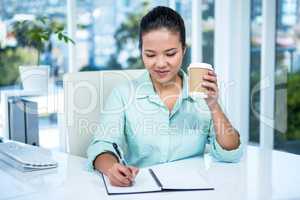 Smiling businesswoman writing notes with a coffee