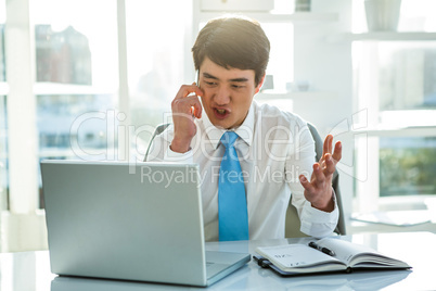 Busy asian businessman working on laptop and calling