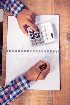 Businessman using calculator while writing on book