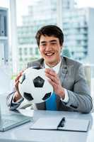 Asian businessman holding soccer ball with thumps up