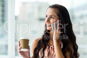 Smiling woman on phone call holding disposable cup