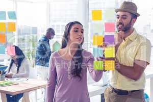 Creative businesswoman writing on adhesive note by colleague
