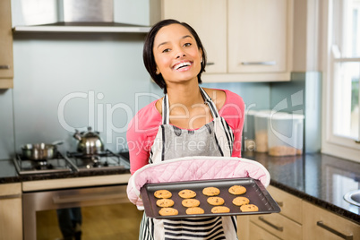 Smiling brunette showing biscuits on baking tin