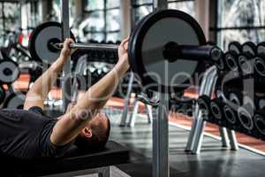 Muscular man lifting barebell while lying on bench