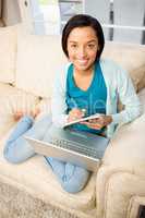 Smiling brunette writing on notepad with laptop on her legs