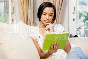 Focused brunette reading a book on the sofa