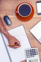 Businessman writing on notebook by coffee at desk