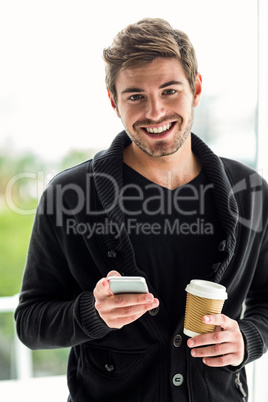 Handsome man using smartphone holding disposable cup