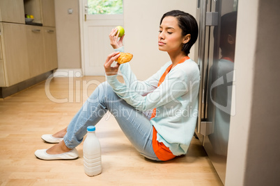 Unsettled brunette holding apple and dessert