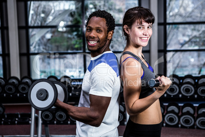 Fit couple lifting dumbbells back to back