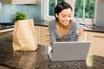 Smiling brunette using laptop and holding credit card