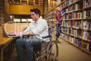 Student in wheelchair typing on his laptop while woman searching