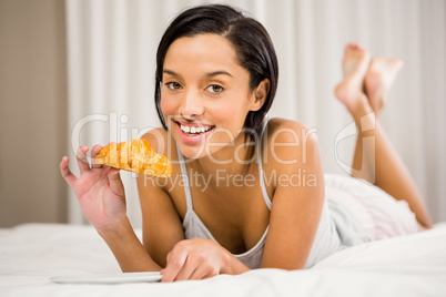 Smiling brunette eating croissant