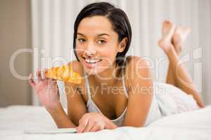 Smiling brunette eating croissant