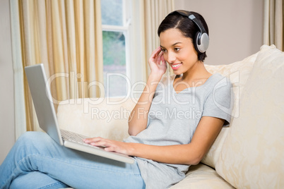 Smiling brunette using laptop and headphones