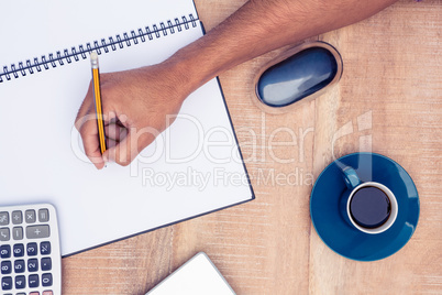 Overhead view of businessman writing on notebook by coffee