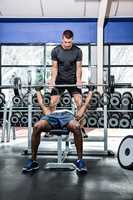 Trainer helping muscular man lifting barebell