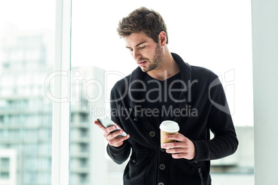 Handsome man using smartphone and holding disposable cup