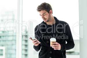 Handsome man using smartphone and holding disposable cup