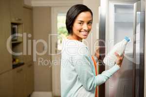 Smiling brunette holding milk bottle with open refrigerator