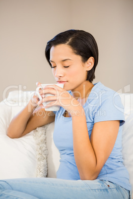 Relaxed brunette drinking by white cup