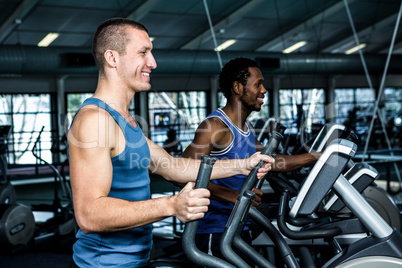 Smiling men using elliptical machine