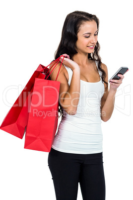 Smiling woman holding shopping bags and using smartphone