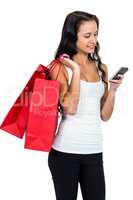 Smiling woman holding shopping bags and using smartphone