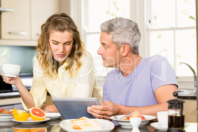 Happy couple using tablet and having breakfast