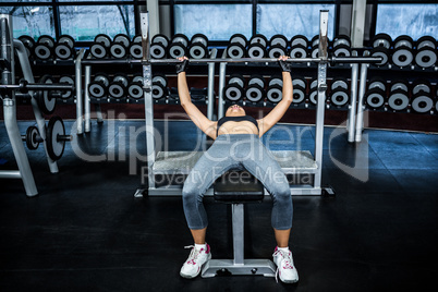Fit woman lifting barbell while lying on bench