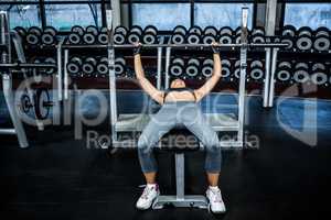 Fit woman lifting barbell while lying on bench