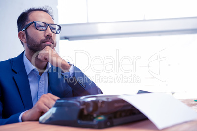 Businessman looking away while working on typewriter