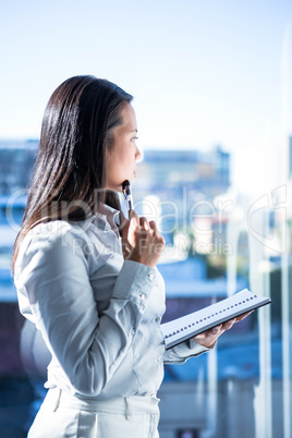 Thoughtful woman with pen on cheek holding notepad