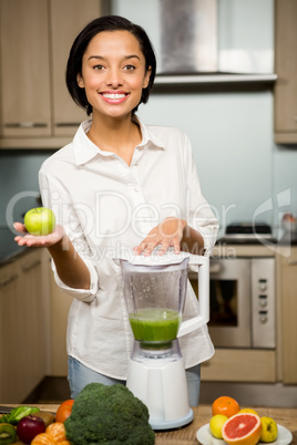 Smiling brunette holding apple and preparing smoothie