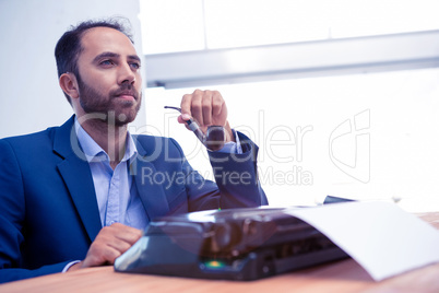 Hipster businessman using typewriter while holding smoking pipe