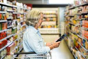 Smiling senior woman with cart using tablet