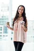 Smiling woman using smartphone holding disposable cup